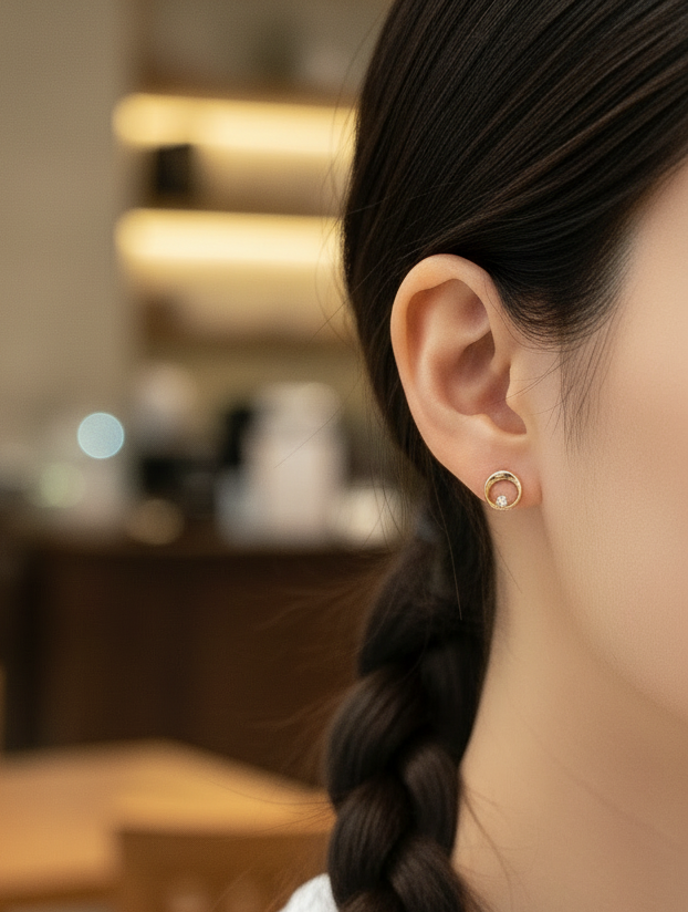 Close-up of a yellow gold ring-shaped earring with a small diamond worn on the ear