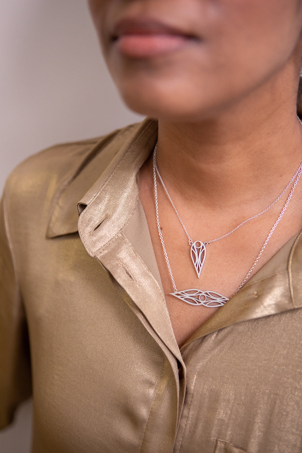 Model in a gold top wearing a sterling silver art deco symmetrical teardrop necklace and matching teardrop pendant necklace.