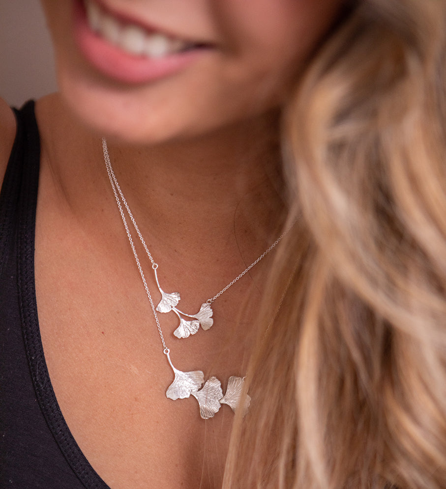 A woman wearing two ginkgo leaf necklaces. The sterling silver leaves are textured and shiny.