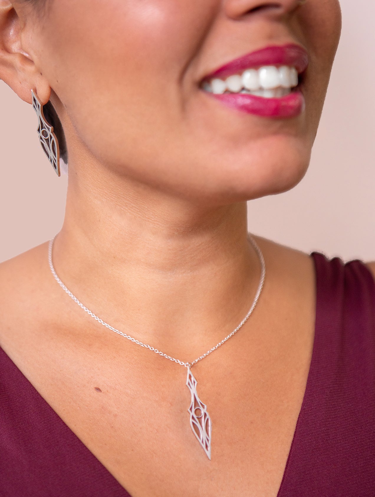 Model in a burgundy dress wearing a geometric art deco pendant necklace and matiching stud earrings.