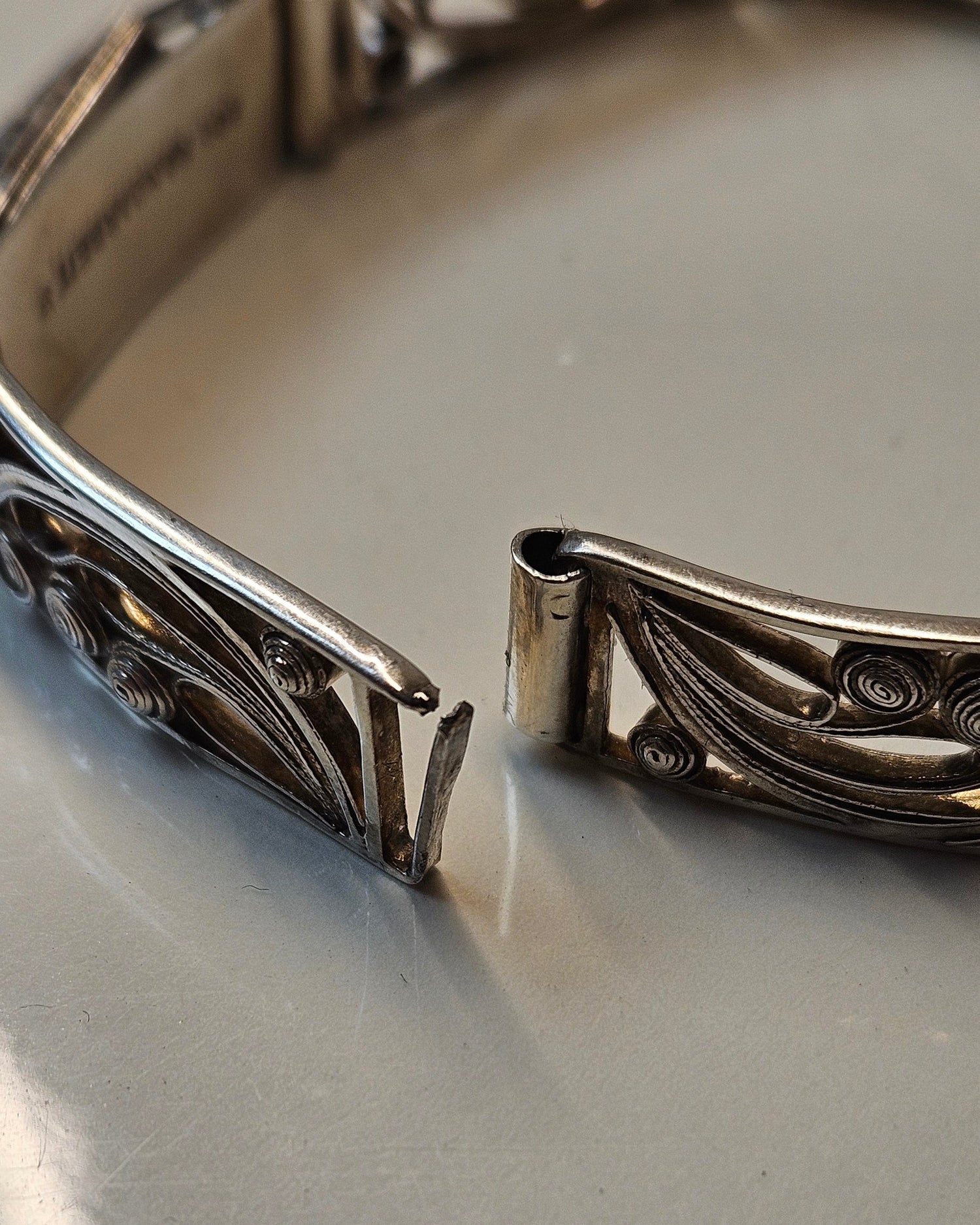 Close-up of a broken silver bracelet with intricate designs the needs jewellery repair.
