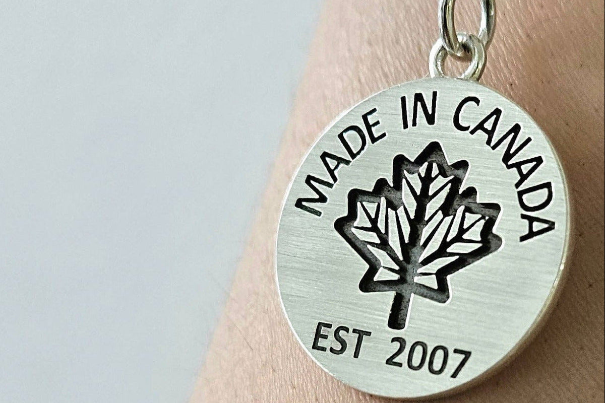 Sterling silver necklace with 'Made in Canada' coin pendant on a silver chain on a person's wrist against a light background