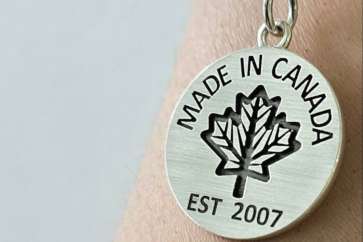 Sterling silver necklace with 'Made in Canada' coin pendant on a silver chain on a person's wrist against a light background