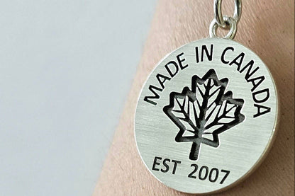 Sterling silver necklace with 'Made in Canada' coin pendant on a silver chain on a person's wrist against a light background