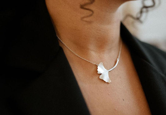 Close up of a large textured ginkgo leaf necklace showing how to wear silver jewelry with a black suit.
