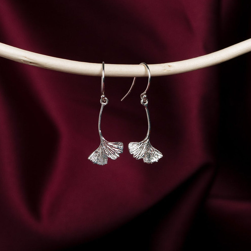 Silver ginkgo leaf earrings on a dark red fabric background