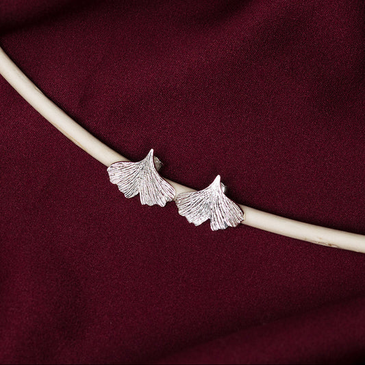 Silver ginkgo leaf earrings on a burgundy fabric background