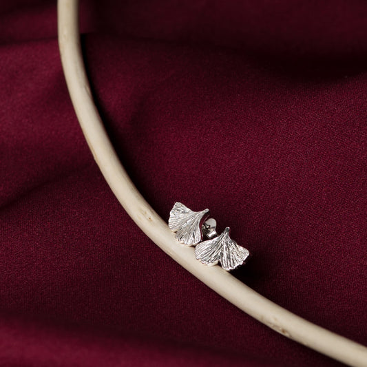 Silver ginkgo leaf earrings on a twig against a burgundy fabric background