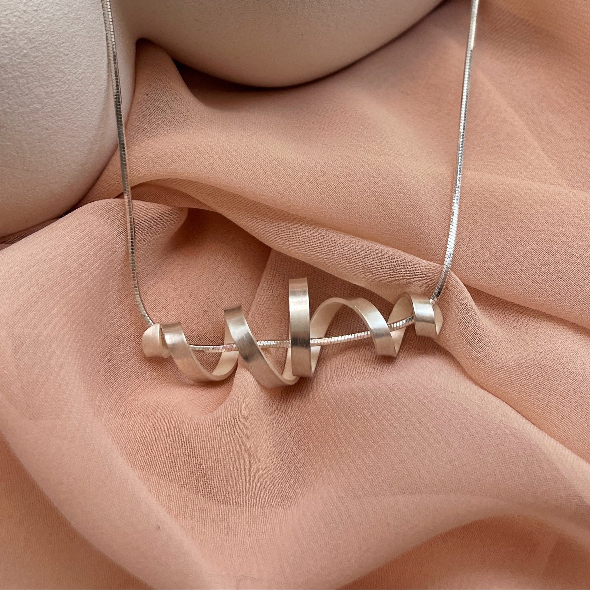 Silver necklace on a soft pink fabric background