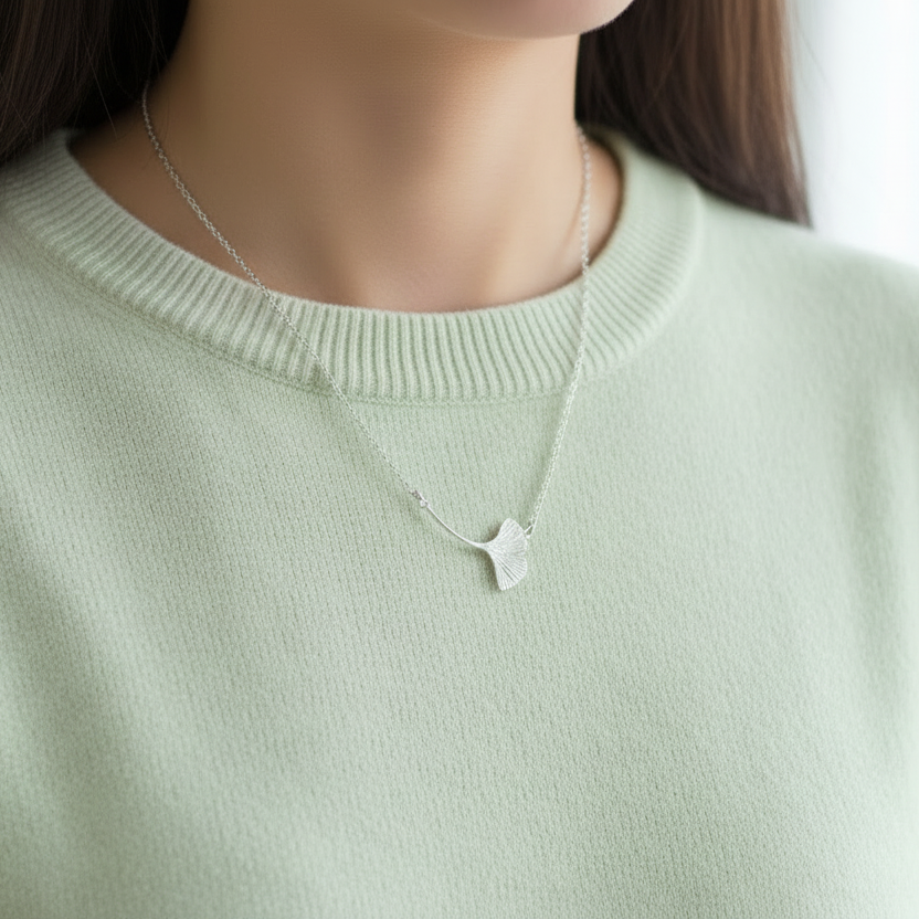 Person wearing a small ginkgo leaf necklace over a light green sweater