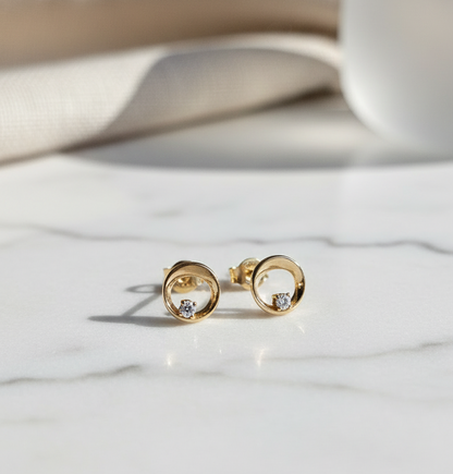 Small 10 karat yellow gold stud earrings with circular design and a diamond inside the bottom rim displayed on a marble surface
