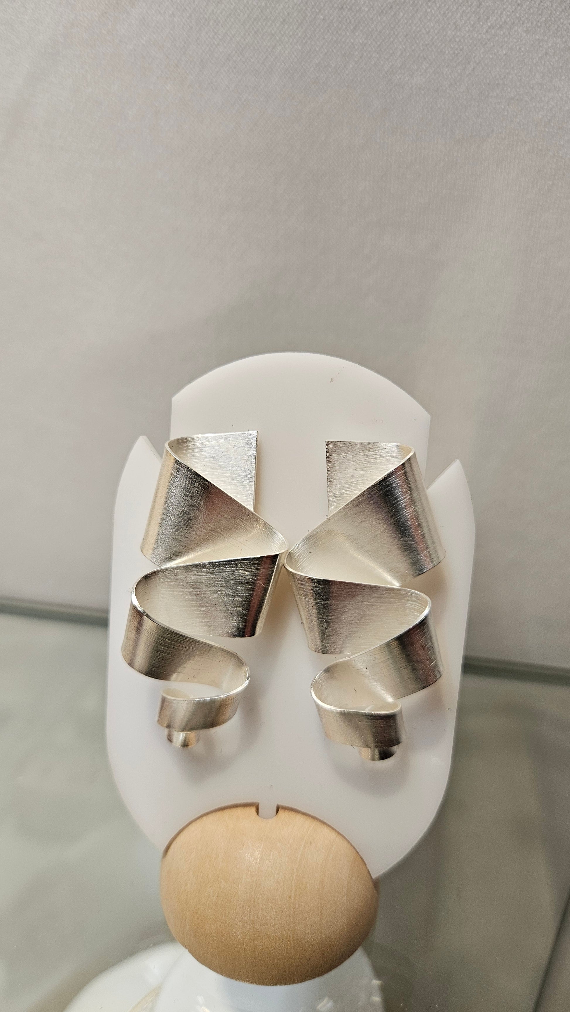 Sterling silver geometric ribbon earrings rippling downward on a white display