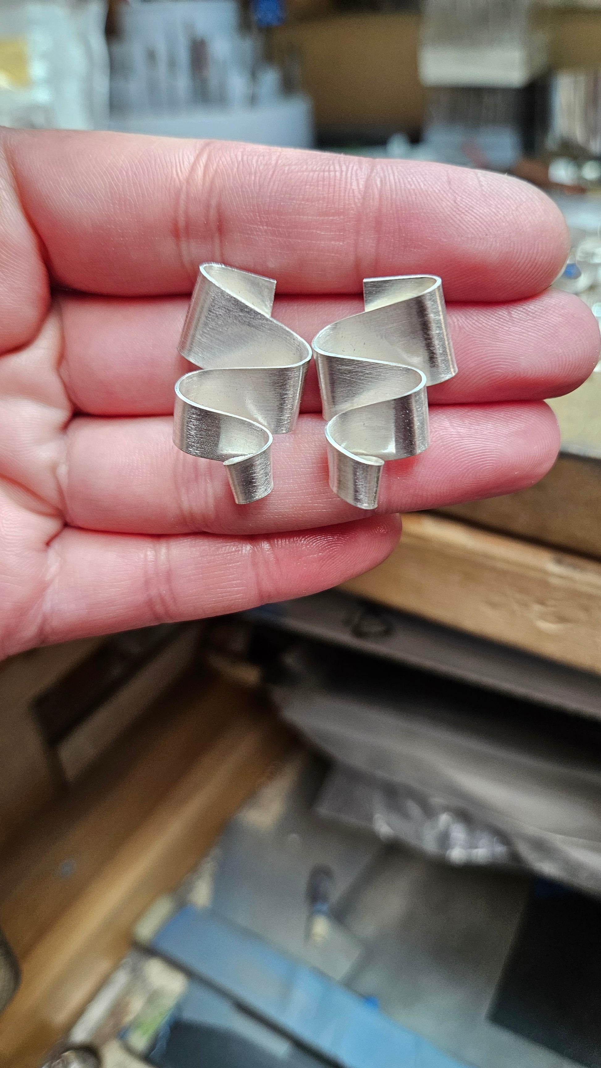 Sterling silver meandering ribbon stud earrings displayed in hand