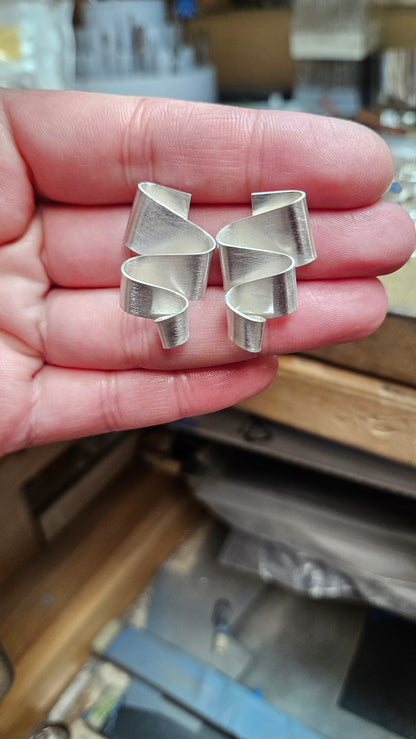Sterling silver meandering ribbon stud earrings displayed in hand