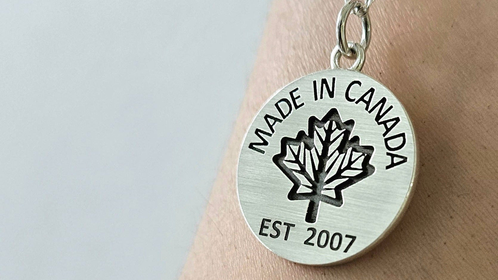 Sterling silver necklace with 'Made in Canada' coin pendant on a silver chain on a person's wrist against a light background