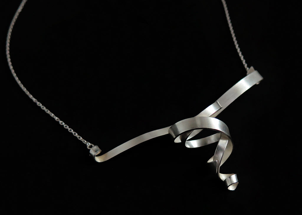 A sterling silver ribbon double spiral pendant necklace with a matte finish and silver chain on a black background.