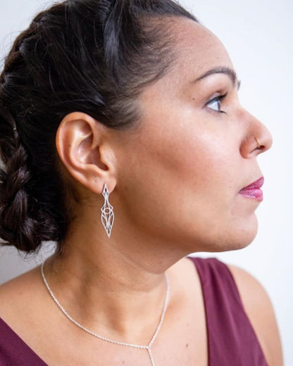 Model in burgundy dress wearing art deco dagger stud earrings.