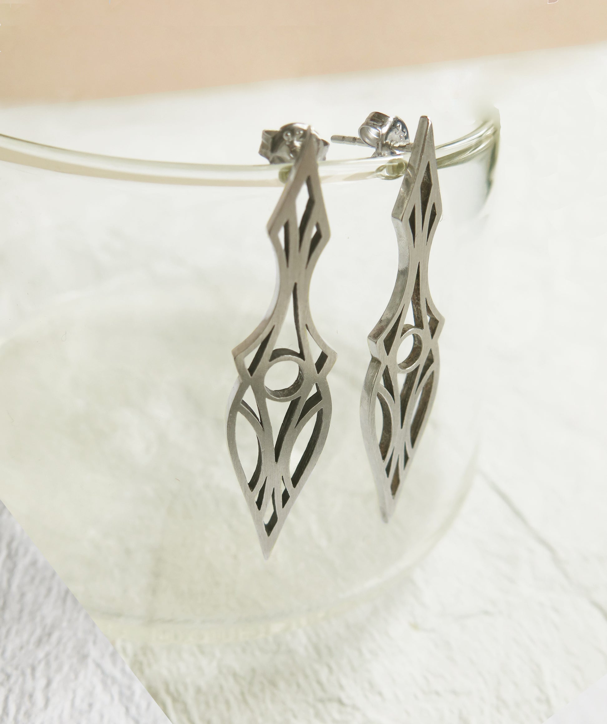 Geometric and symmetrical art deco dagger stud earrings hanging on a glass rim.