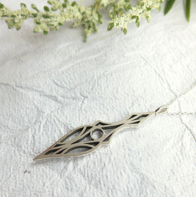 Geometric and symmetrical art deco dagger pendant necklace. Made of brushed sterling silver and oxidized for contrast. On a textured white paper background.