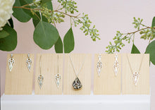 Load image into Gallery viewer, A collection of sterling silver geometric art deco teardrop and dagger jewellery on pale wood panels. From left to right: teardrop stud earrings, teardrop hoop earrings, fig pendant necklace, dagger stud earrings, and teardrop pendant necklace. With flowers and leaves behind.

