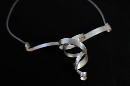 An elegant and modern matte finish sterling silver double whirl ribbon necklace on a silver chain.