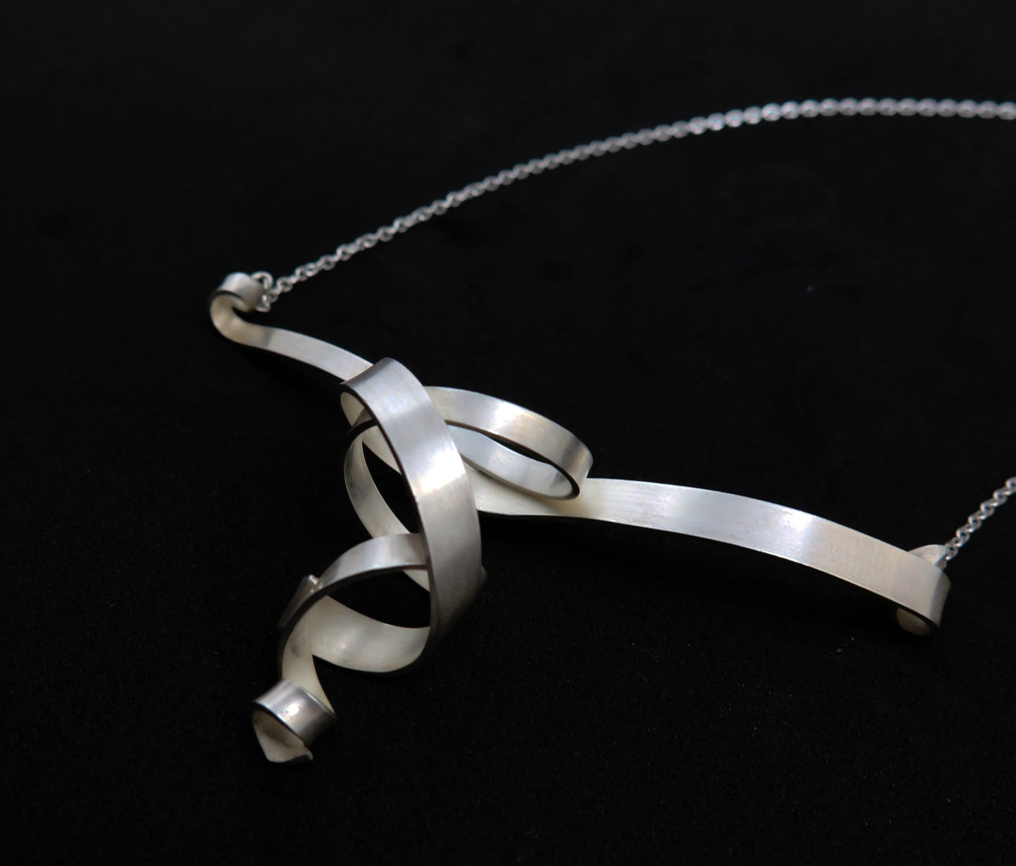 A double helix spiral necklace in sterling silver with a matte finish on a silver chain.