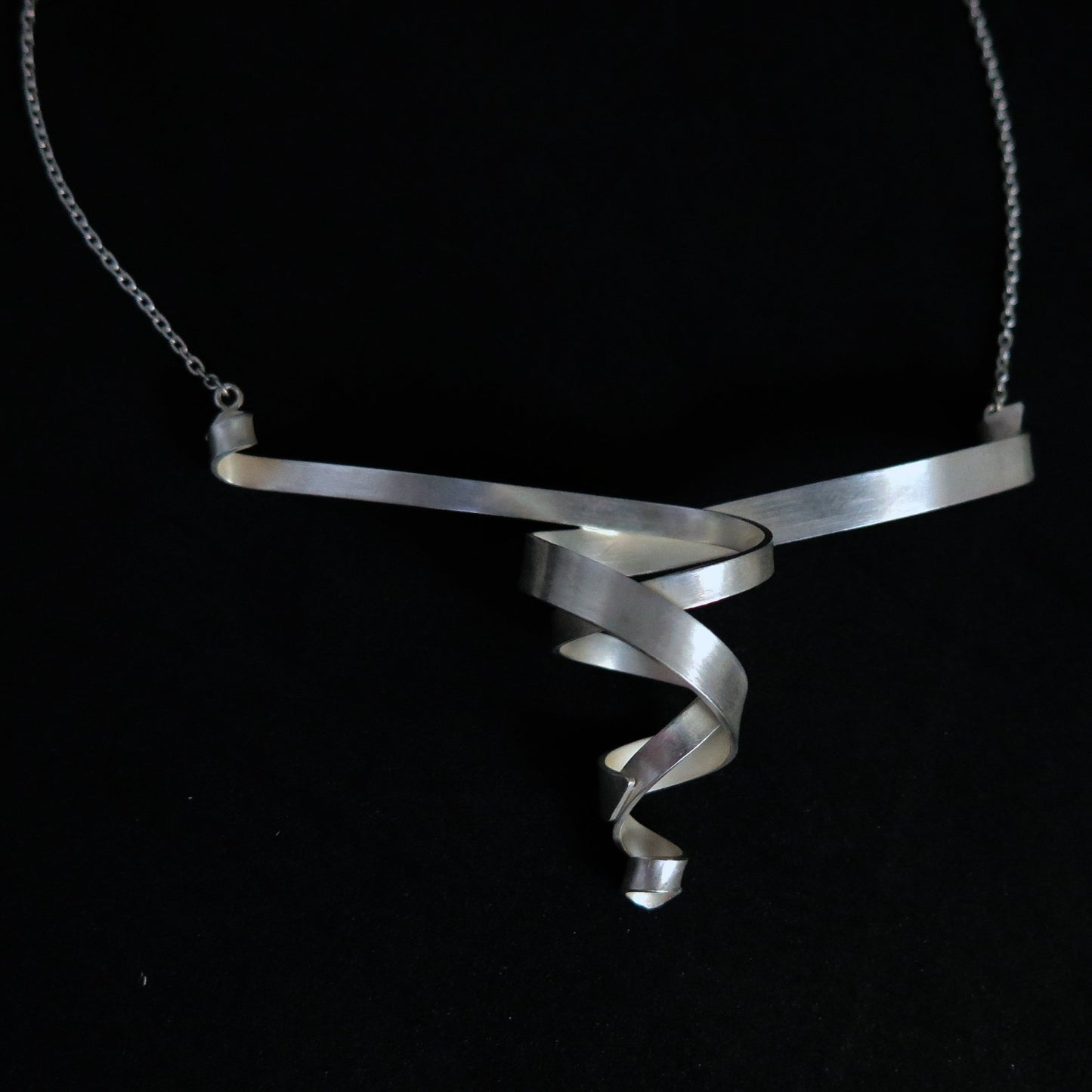 A modern sterling silver helix spiral ribbon pendant necklace on a black background.