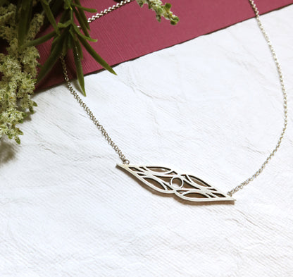 Art deco double teardrop symmetrical sterling silver necklace in high-sheen brushed finish oxidized for contrast. On a silver chain. On white and burgundy textured paper and a sprig of flowers.
