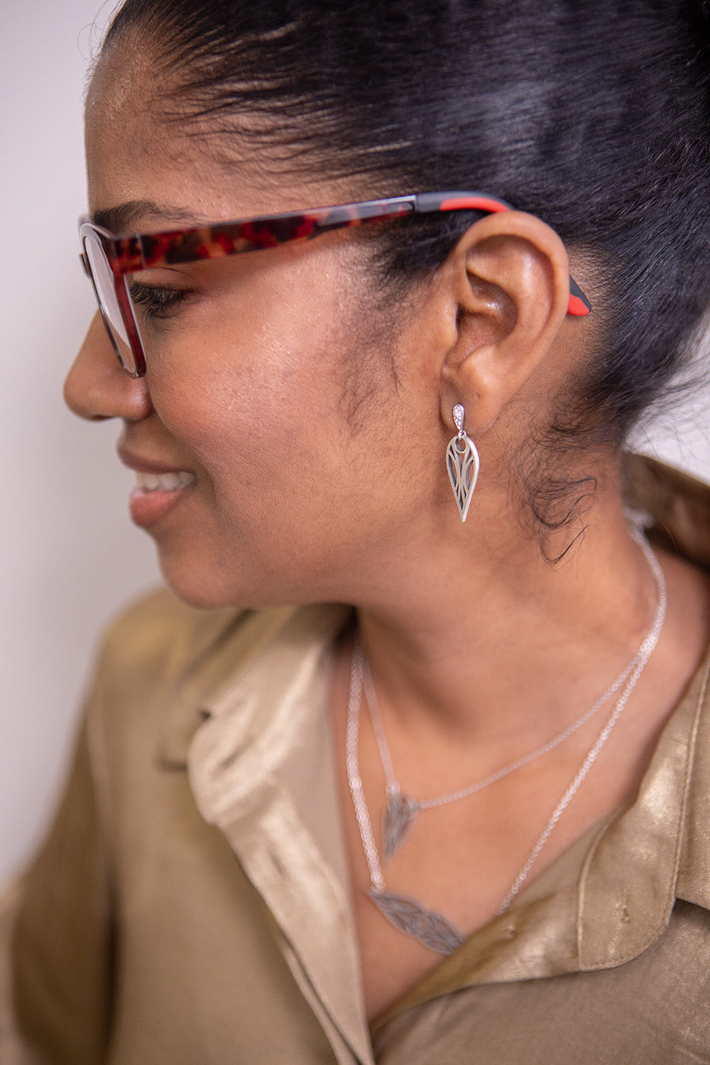 Model in a gold top and glasses wearing sterling silver art deco teardrop stud earrings and matching teardrop pendant necklace and symmetrical teardrop necklace.