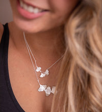 Load image into Gallery viewer, A woman wearing two ginkgo leaf necklaces. The sterling silver leaves are textured and shiny.
