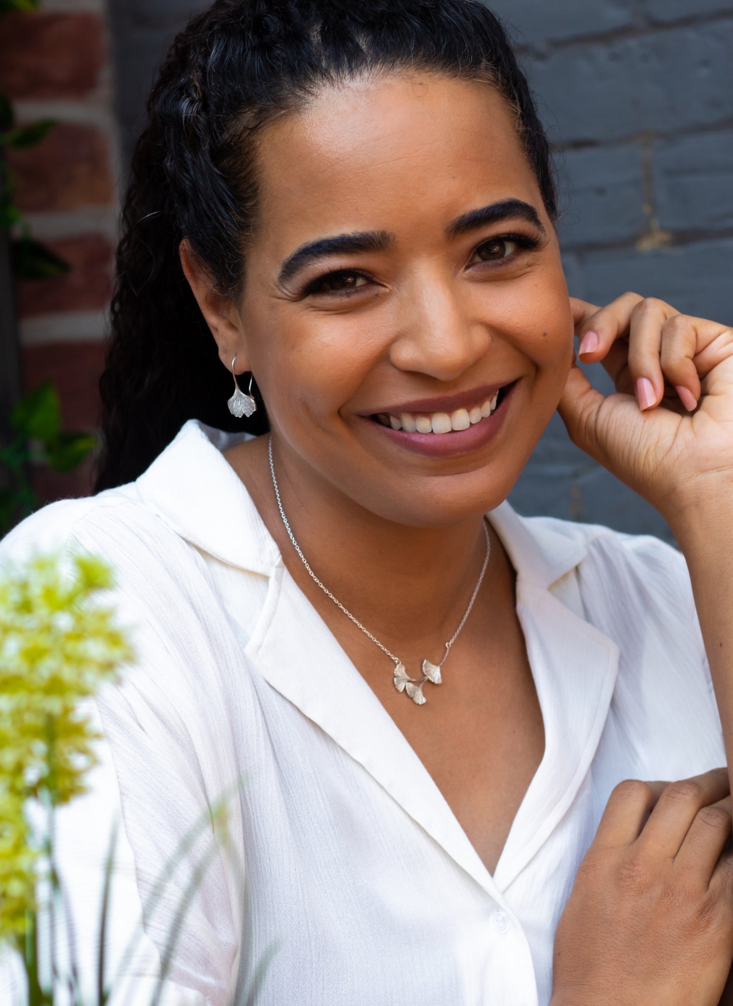 A smiling woman wearing ginkgo leaf dangle earrings and a necklace with three small ginkgo leaves