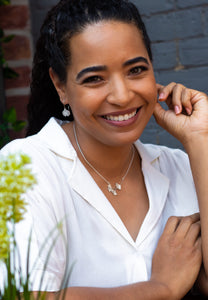 A smiling woman wearing ginkgo leaf dangle earrings and a necklace with three small ginkgo leaves