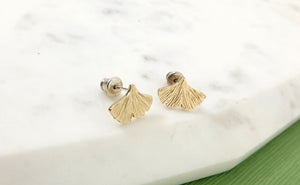 Textured gold ginkgo leaf earrings resting on a piece of marble